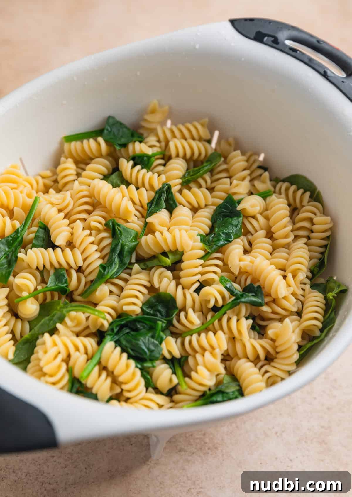 Cooked rotini pasta in colander with wilted spinach.