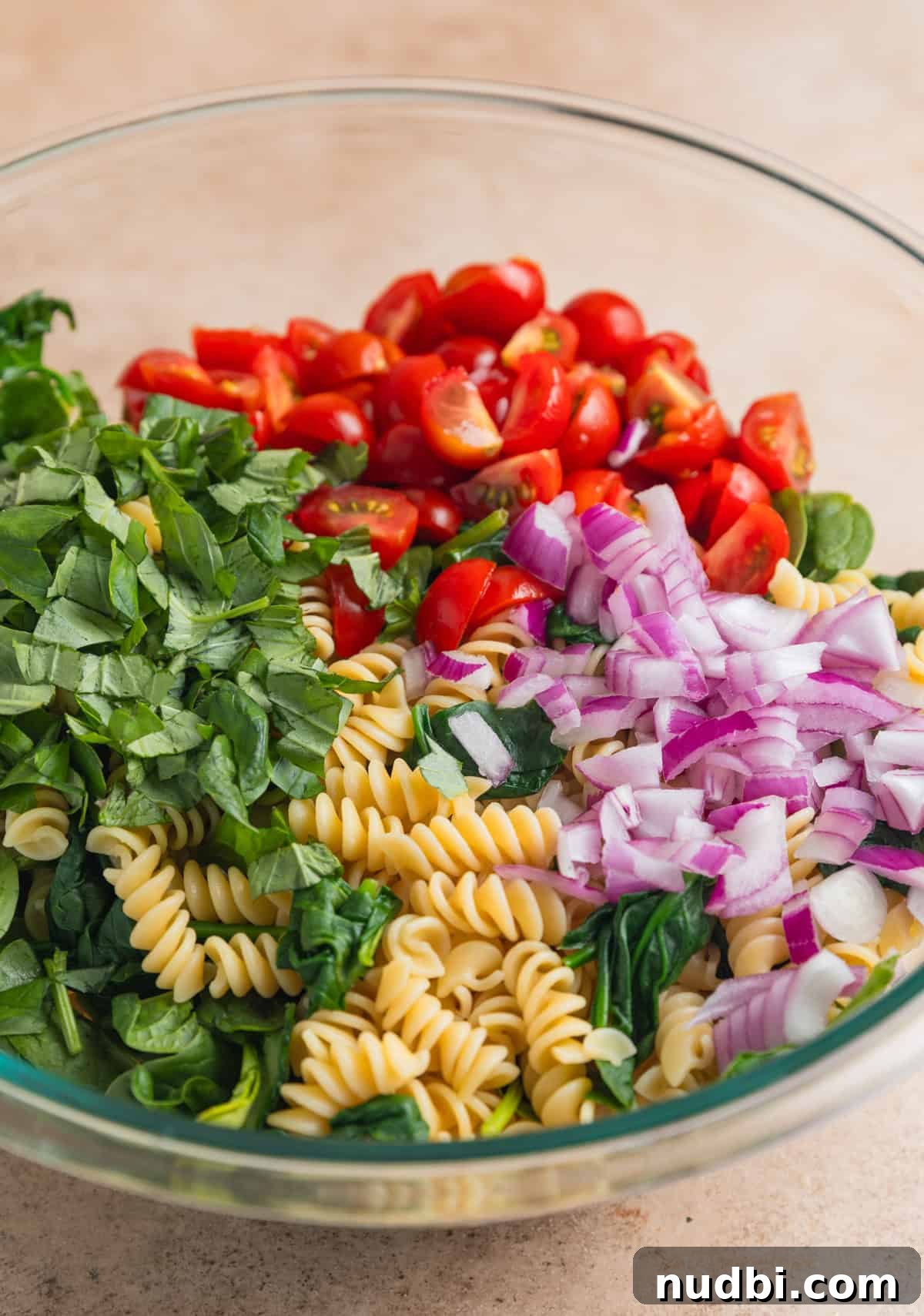 Large mixing bowl with pasta, spinach, chopped basil, tomatoes and onion.