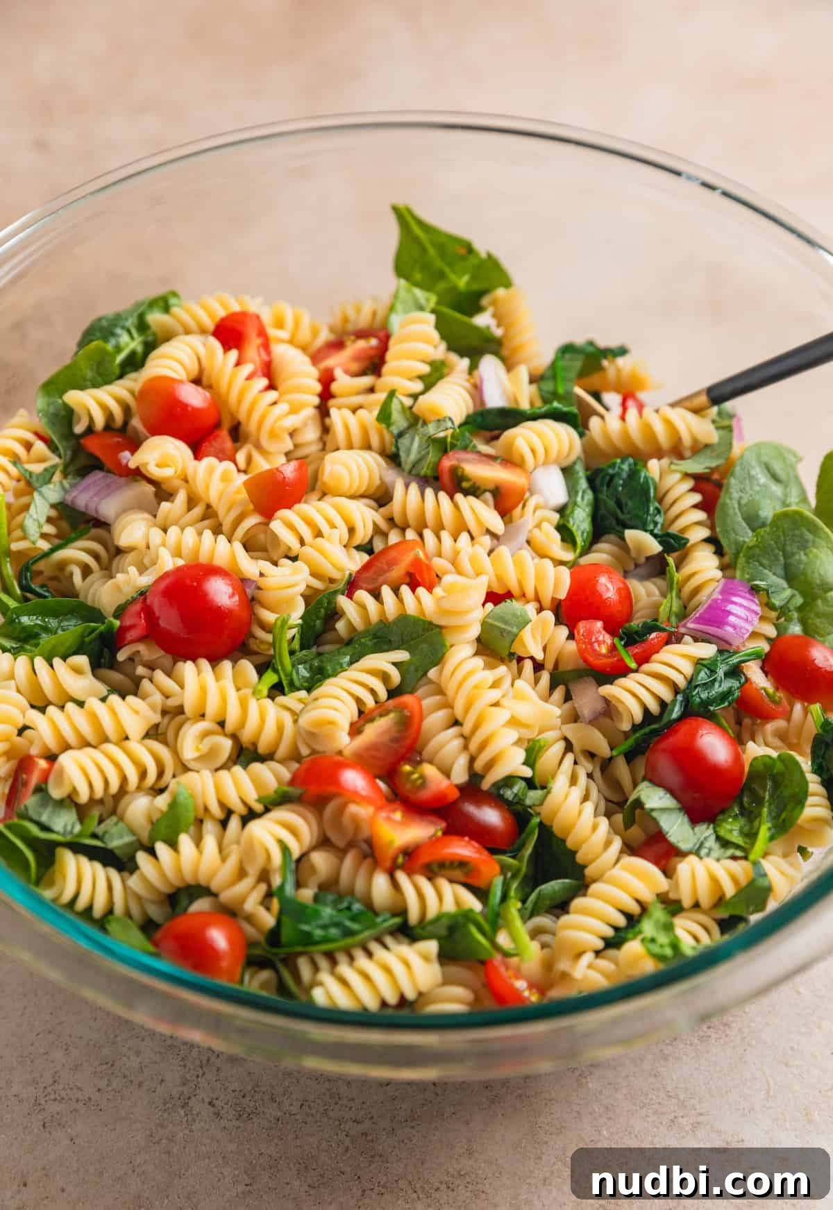 Tomato basil pasta salad ingredients tossed together in bowl.