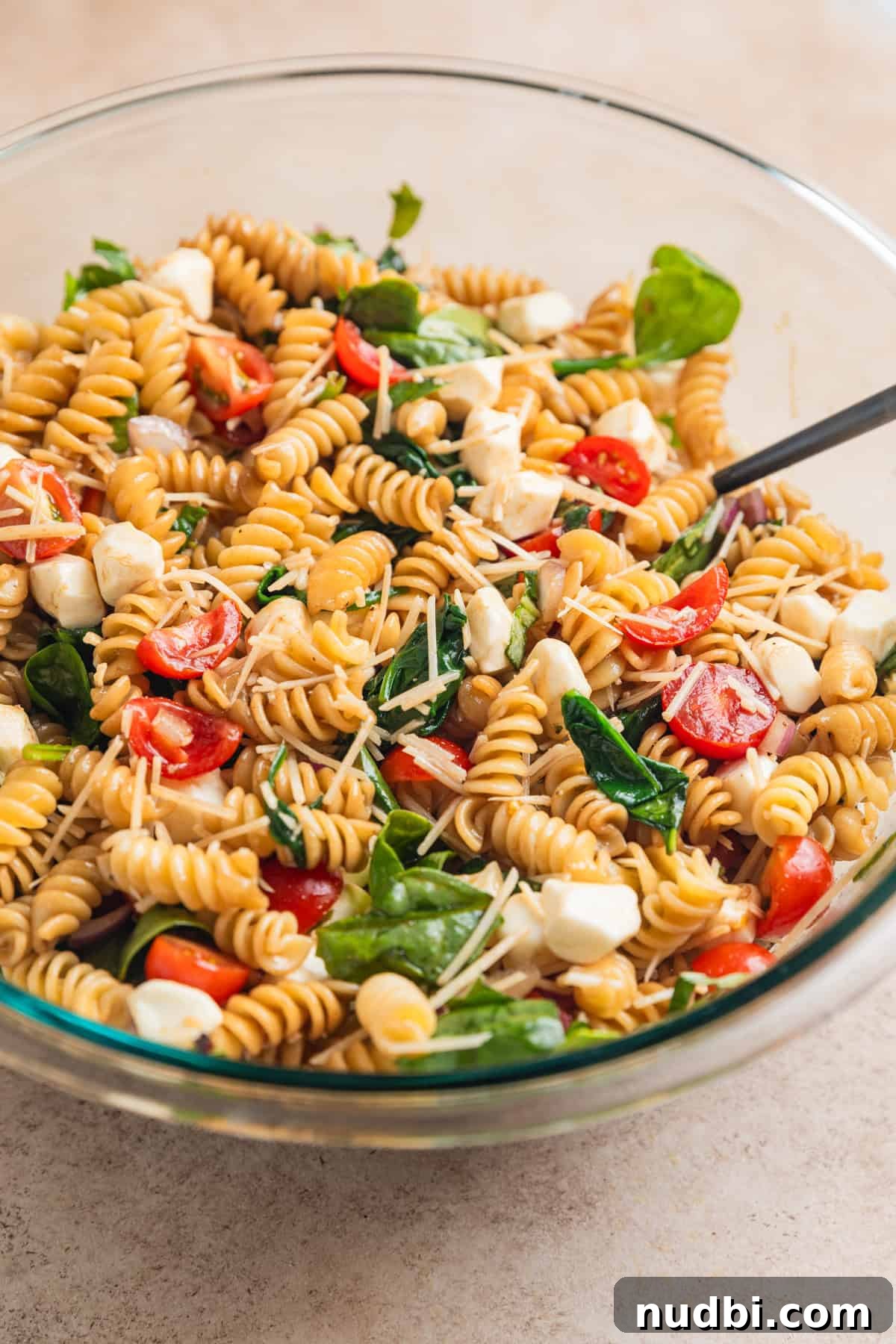 Pasta salad mixture tossed with dressing in bowl with spoon.