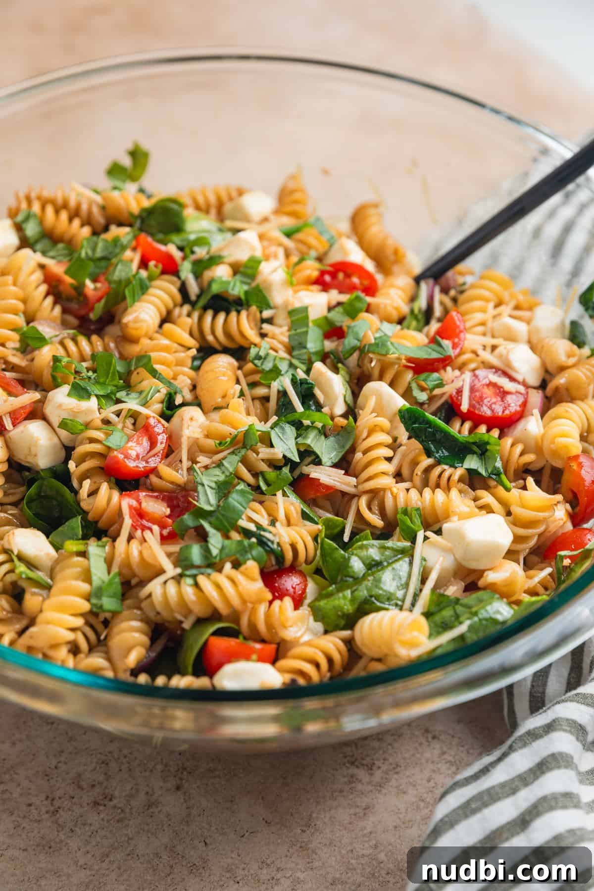 Prepped pasta salad with basil, tomatoes, mozzarella, spinach and other ingredients in bowl.