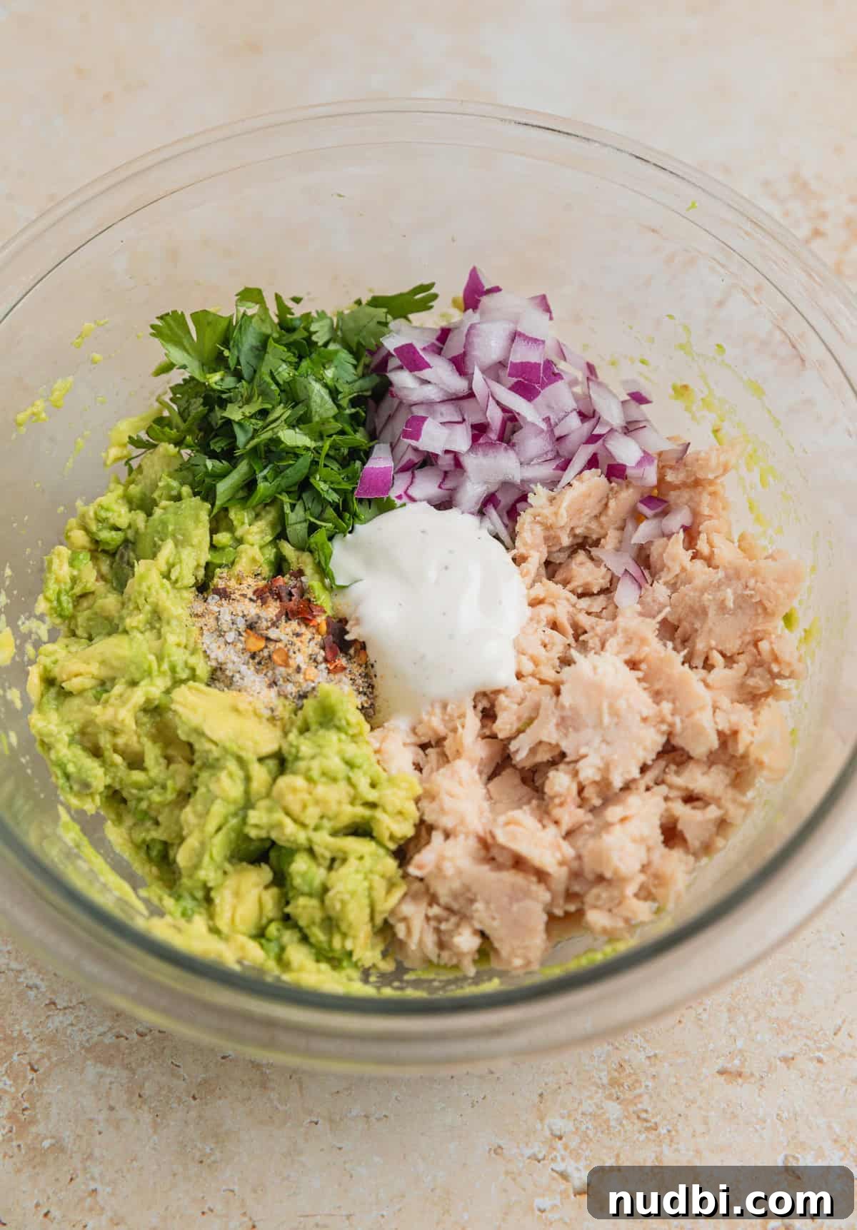 Creamy Avocado Ranch Tuna Salad with Fresh Herbs 5 Flaked tuna, red onion, cilantro, avocado and Ranch dressing in mixing bowl before being stirred.