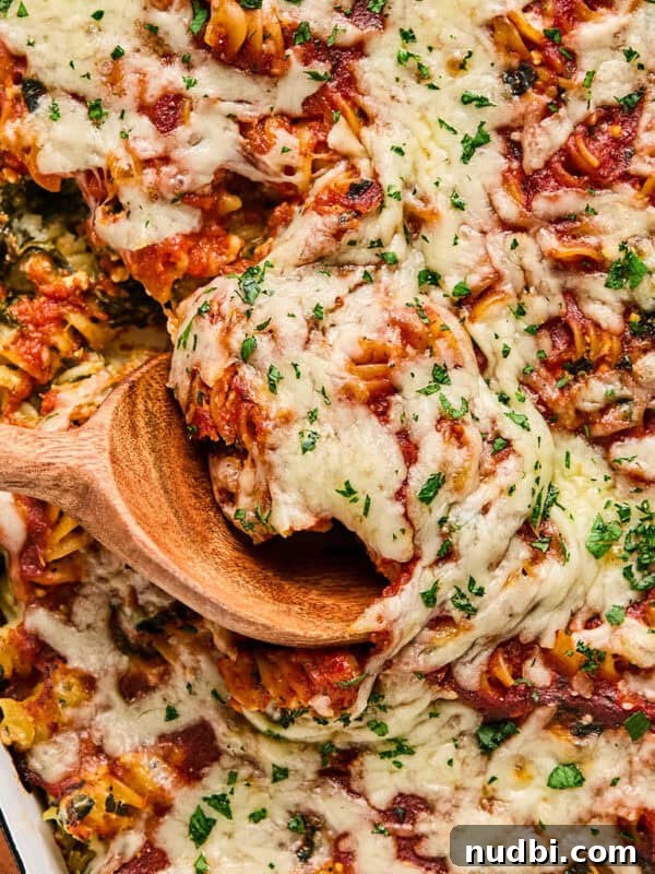 Creamy Spinach and Ricotta Tortellini Bake 12 Wooden spoon scooping into pasta topped with mozzarella cheese and parsley.