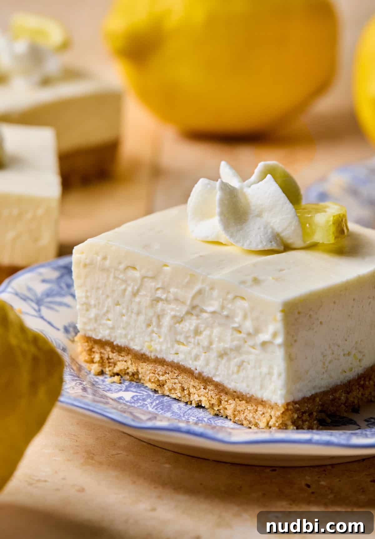No-Bake Lemon Cheesecake Bars with Zesty Graham Crust 2 Lemon cheesecake bar on plate with whipped cream and lemon slice on top.