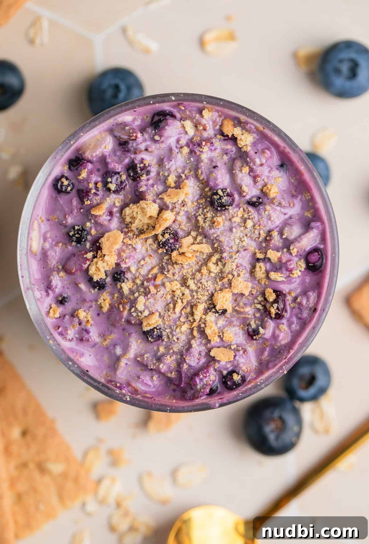 Creamy Blueberry Cheesecake Overnight Oats Recipe 2 Overhead view of blueberry cheesecake overnight oats in glass topped with crushed graham crackers.