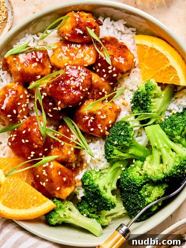 Spicy orange chicken over rice with broccoli and orange slices.