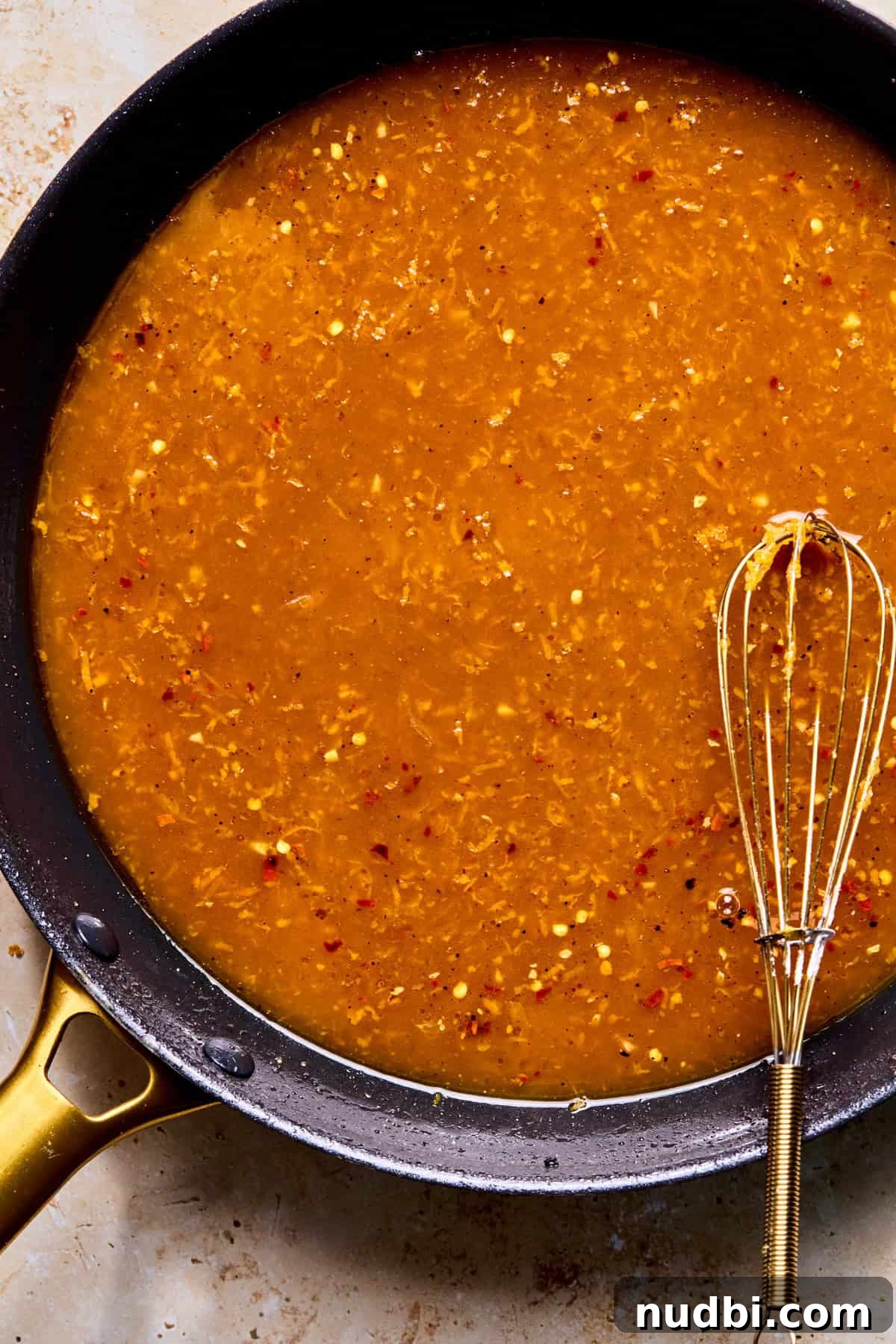 Crispy Spicy Orange Chicken with Tangy Sauce 10 Spicy orange sauce in skillet with whisk before thickening.