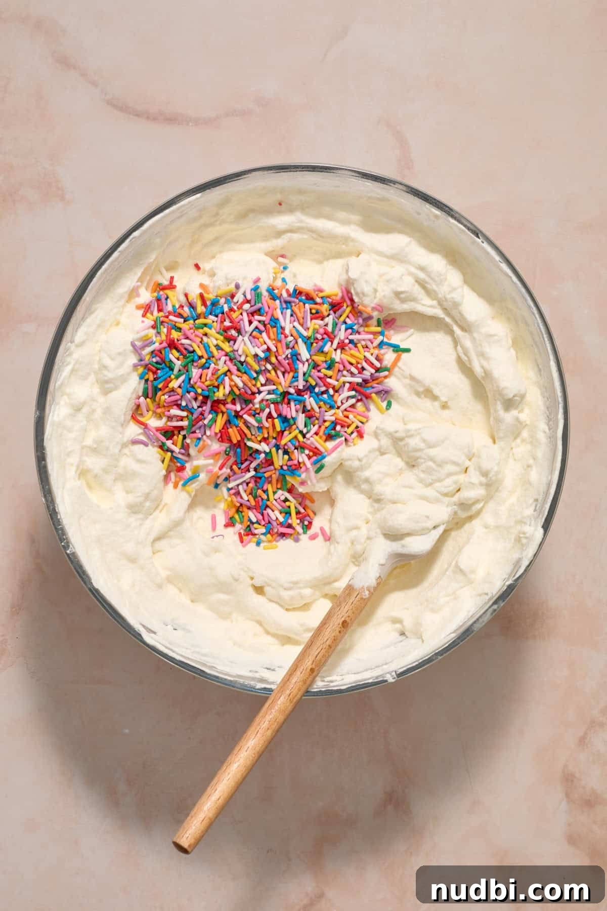 No-Bake Funfetti Icebox Cake Recipe with Whipped Frosting 7 Sprinkles added to cream cheese and whipped cream mixture in bowl.
