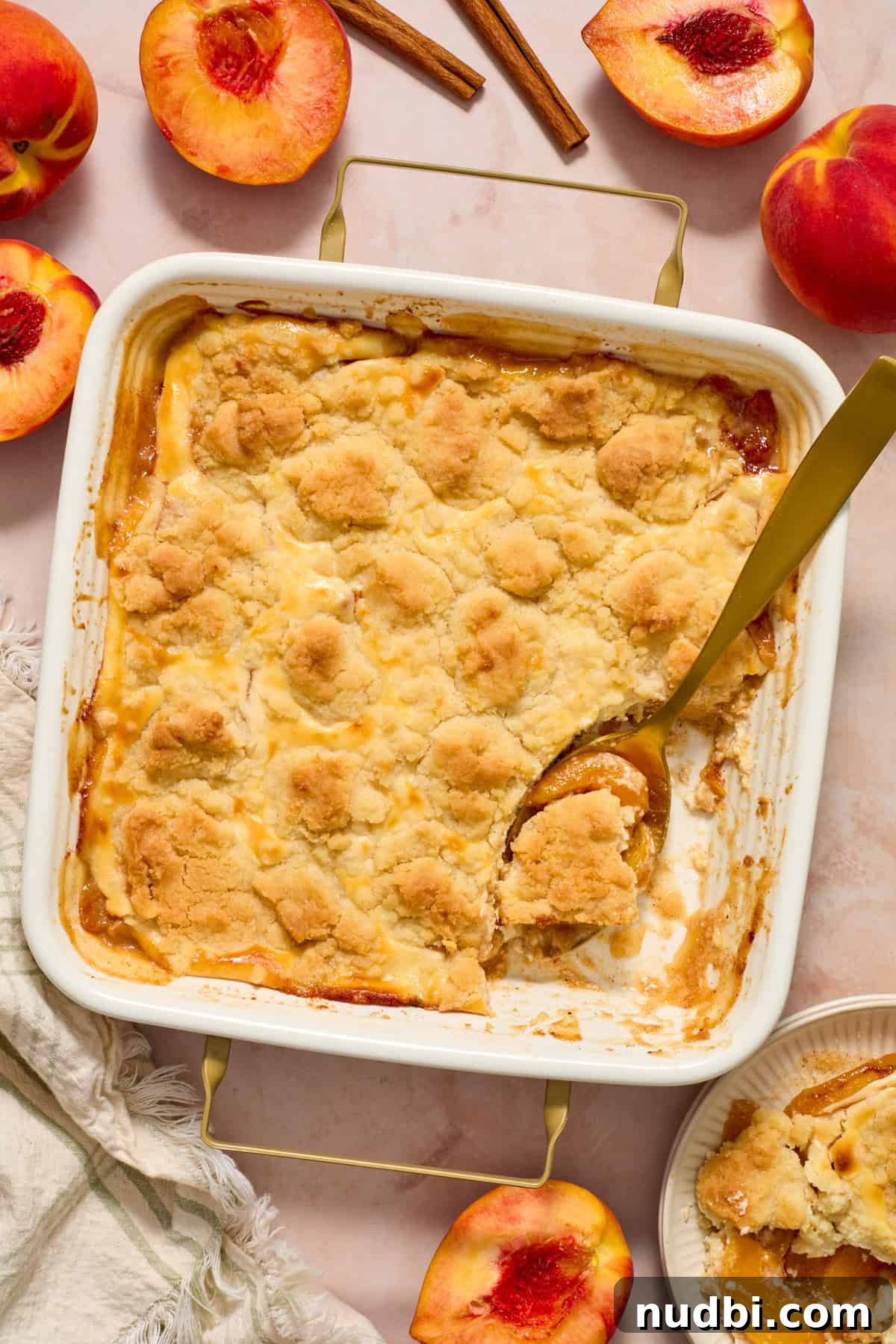 Cream Cheese Peach Cobbler with Buttery Biscuit Topping 11 Peach cobbler cheesecake dessert in pan with serving spoon.