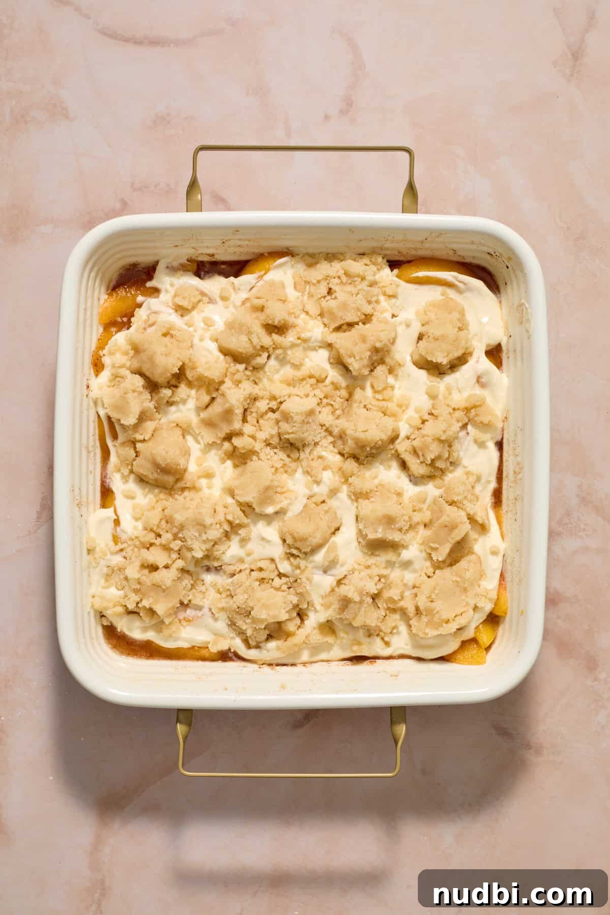 Cream Cheese Peach Cobbler with Buttery Biscuit Topping 9 Cobbler crumbles sprinkled over peach and cheesecake layer before baking.