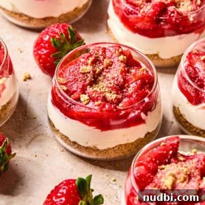 Dessert glass with layered strawberry topped cheesecake cups.