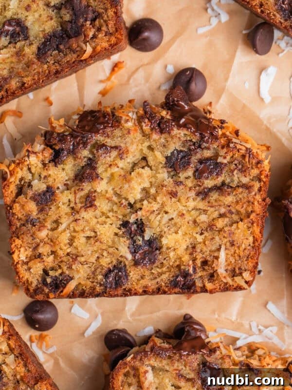 Slice of coconut banana bread with melty chocolate chips on parchment paper.