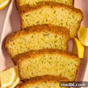 Slices of lemon glazed lemon zucchini bread on plate with lemon wedges.