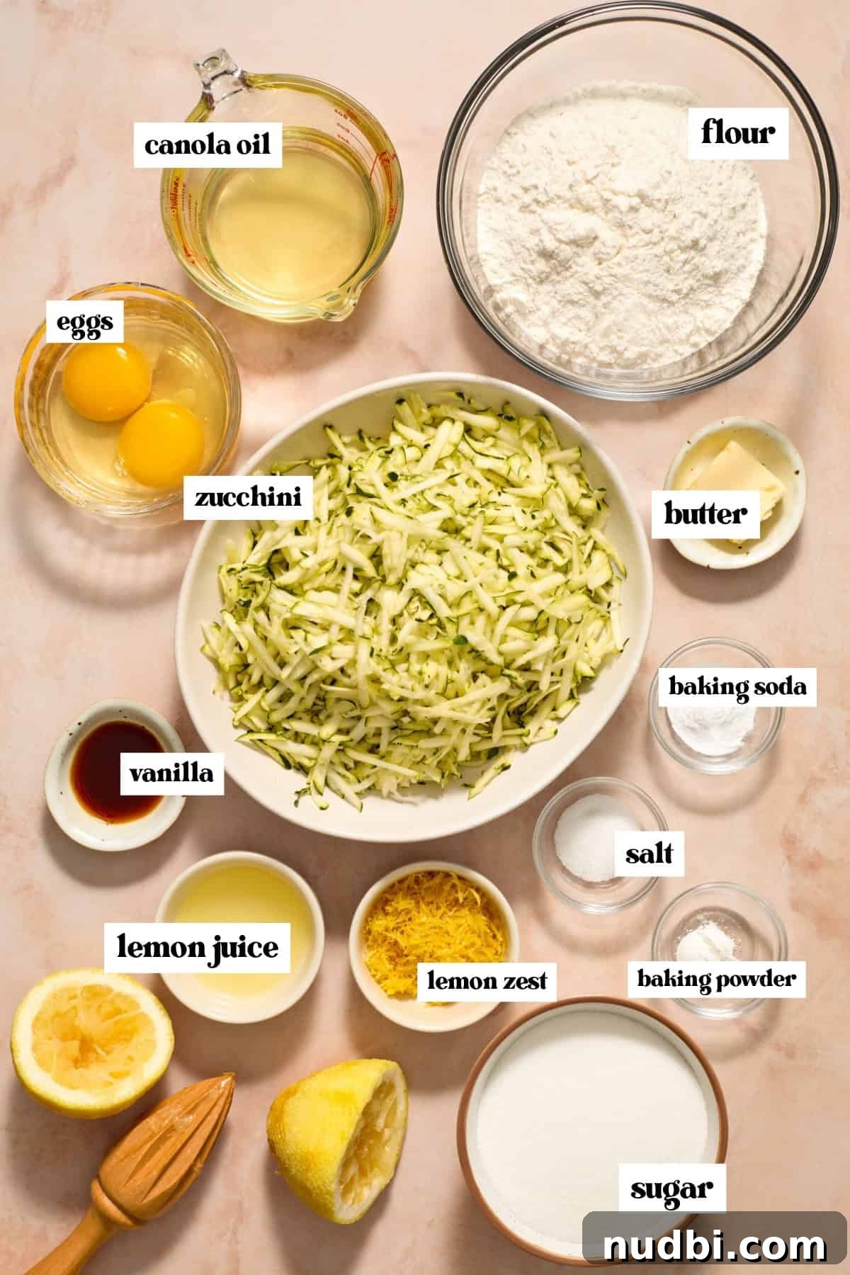 Shredded zucchini, sugar, flour, eggs and other labeled ingredients prepped for recipe.