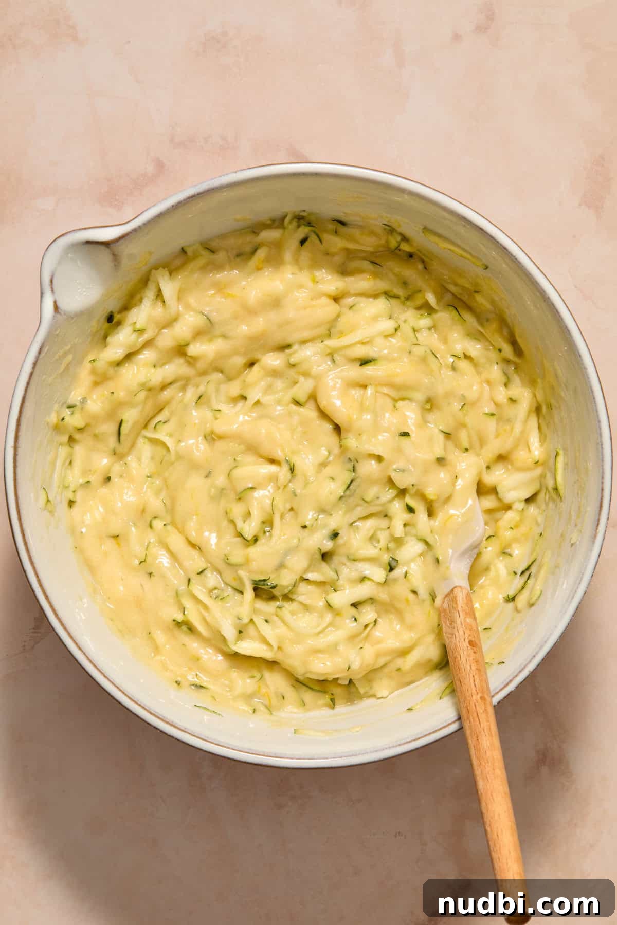 Zucchini folded into batter in bowl with spatula.